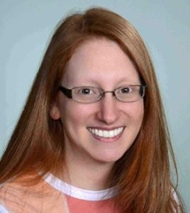 A headshot showing a woman with long red hair and glasses