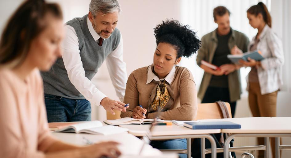A teacher leans over a student's desk, helping them