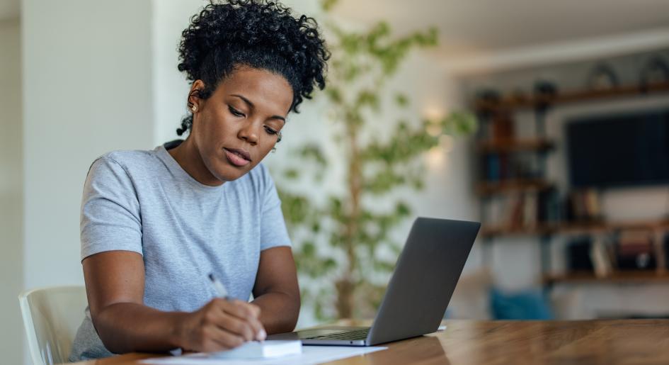 A woman writes on a notepad next to a laptop